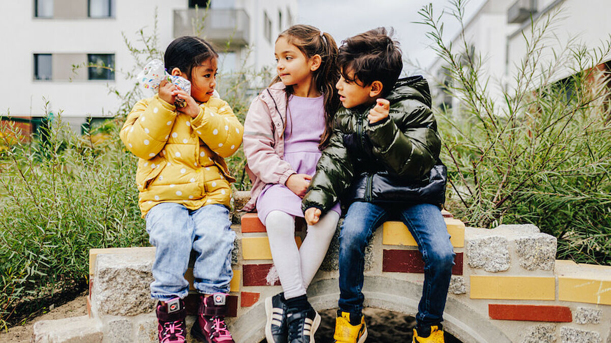 Drei Kita-Kinder sitzen auf einer Mauer