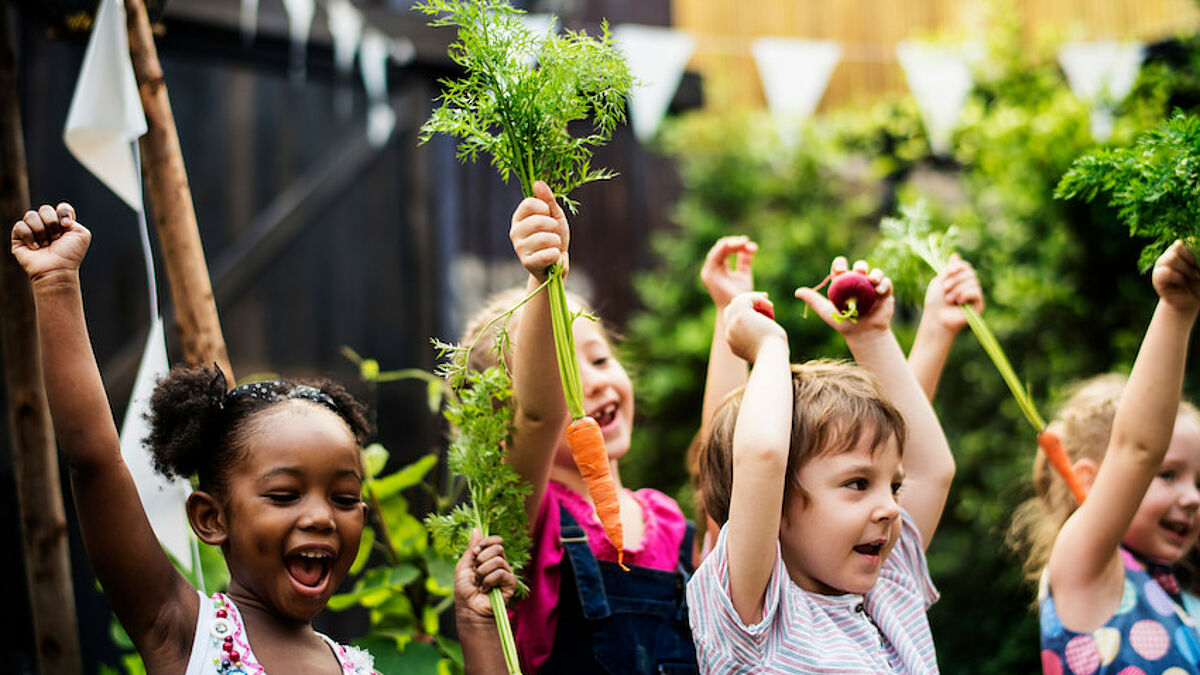 Kinder in einem Garten halten fröhlich Möhren in die Luft.