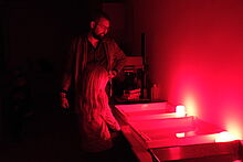 Dominik Grübl unterstützt ein Kind dabei, ein Foto in einer Dunkelkammer zu entwickeln.