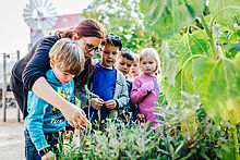Erzieherin und Kinder betrachten Pflanzen im Garten