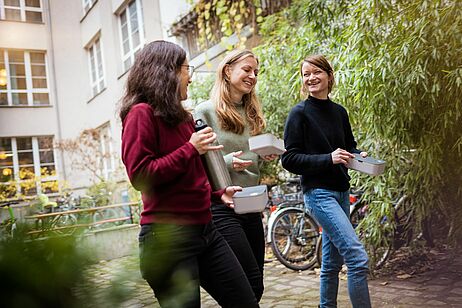 Drei junge Frauen laufen mit einer Lunchbox über den Innenhof