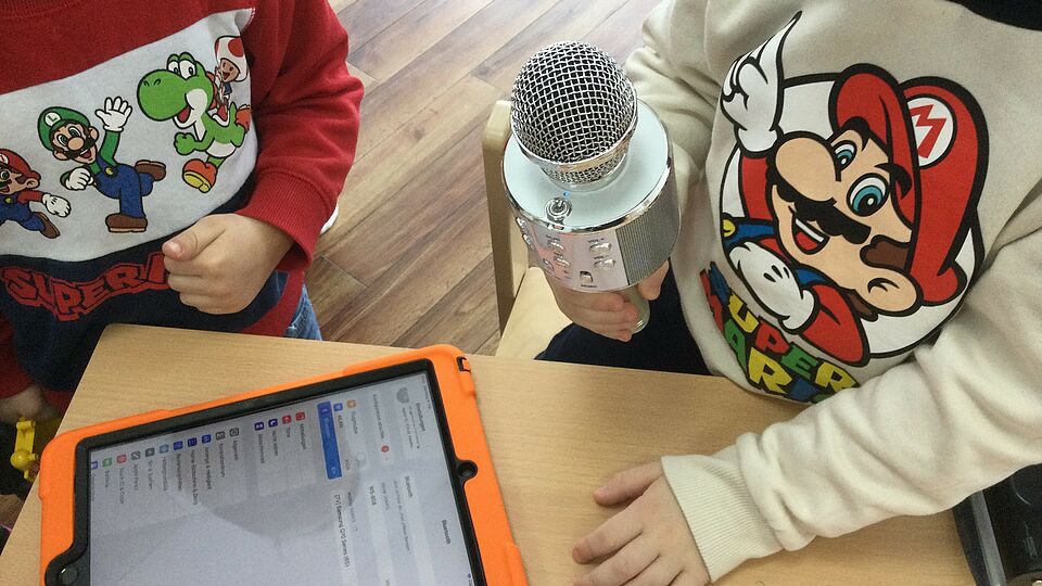 Zwei Kinder nehmen ihre Stimmen mit dem Mikrofon auf einem Tablet auf.