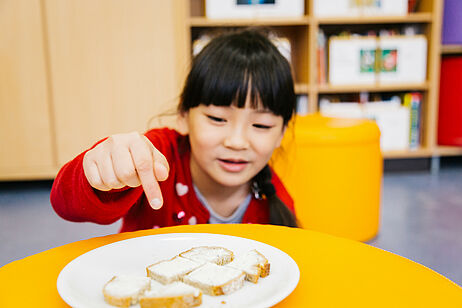 Kind zählt Brotscheibe vor sich, die in sechs Stücke zerschnitten ist