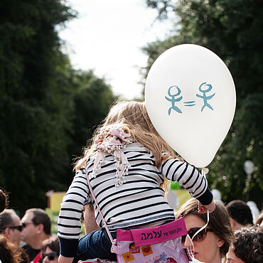 Ein Kind sitzt auf Schultern und hält einen Luftballon in der Hand