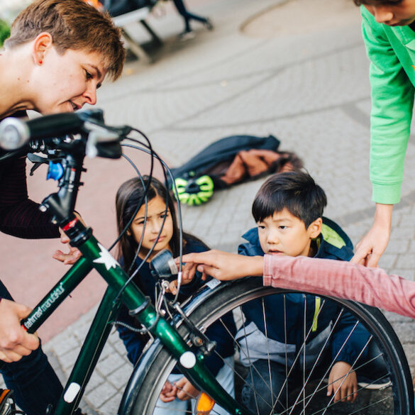 Eine Lernbegleitung erforscht auf dem Schulhof mit vier Kindern im Grundschulalter ein Fahrrad. Gemeinsam betrachten sie die Frontleuchte des Rads.