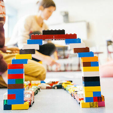 Kinder spielen mit einer Brücke aus Legosteinen.