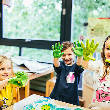 Kinder halten ihre grün bemalten Hände in die Luft