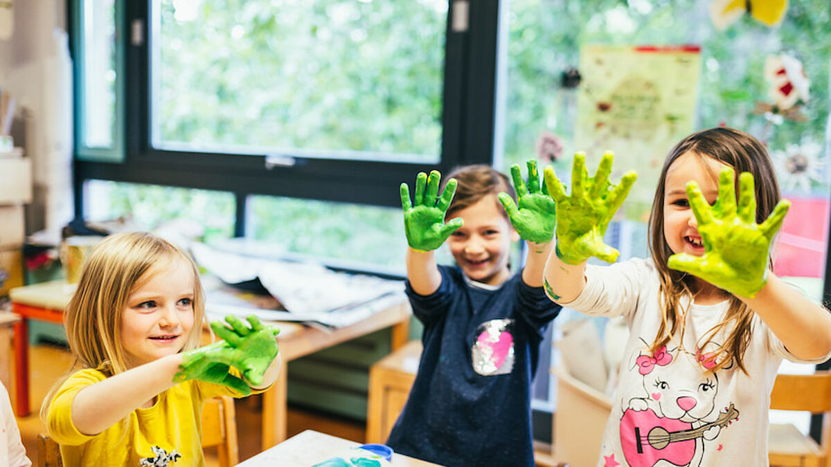 Kinder halten ihre grün bemalten Hände in die Luft