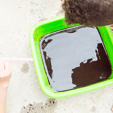 Ein Kind pustet in einen Behälter mit schmutzigem Wasser