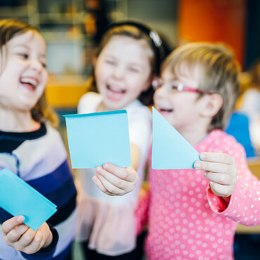 Drei Kinder halten jeweils einen blauen Zettel vor sich